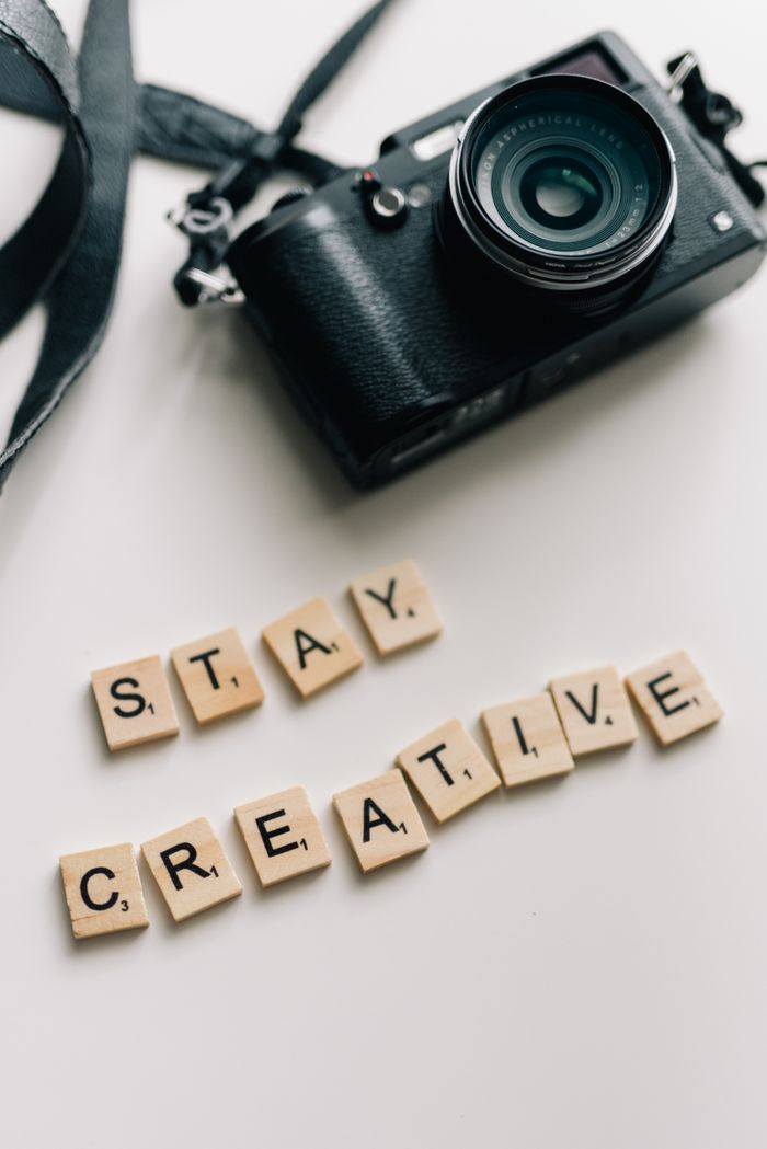 About Creative photo of camera and tiles spelling 'Stay Creative' on white background.